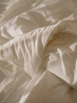 Close-up of crumpled white bed linen with soft natural lighting, evoking coziness.