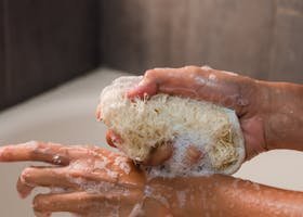 Detailed image of hands using a loofah with soap bubbles for personal hygiene.